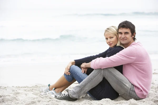 年轻夫妇坐在冬季海滩上的假期 — 图库照片