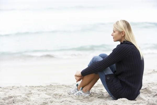 Junge Frau im Urlaub sitzt am Winterstrand — Stockfoto