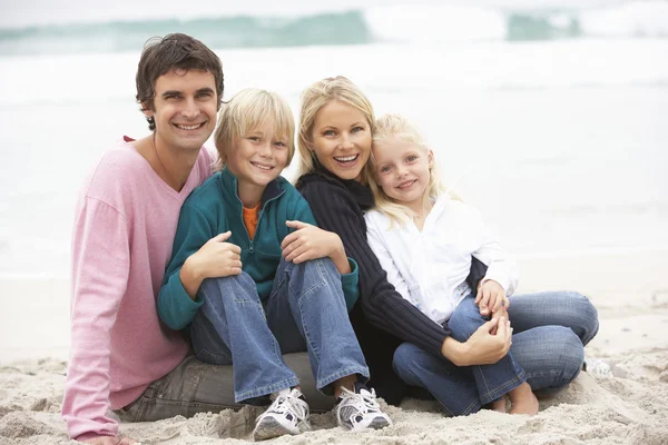 坐在冬季海滩上的年轻家庭 — 图库照片