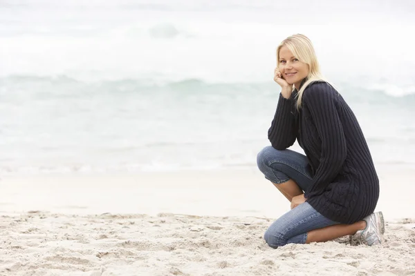 休日は冬の浜辺にひざまずいて若い女性 — ストック写真