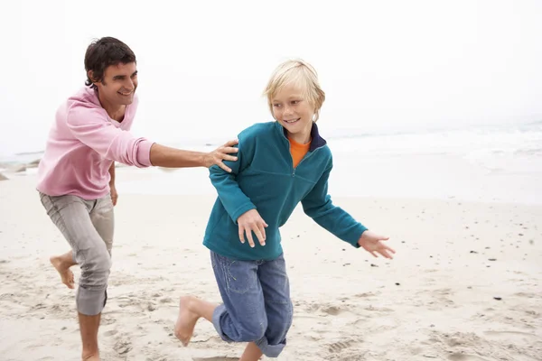 Padre persiguiendo hijo a lo largo de invierno playa — Foto de Stock