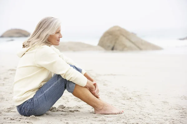Starszy kobieta siedzi na plaży zimowych wakacji — Zdjęcie stockowe