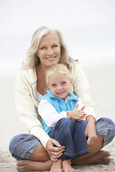 Grootmoeder en kleindochter op vakantie zittend op winter strand — Stockfoto