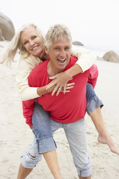 Senior man geven vrouw piggyback op winter strand — Stockfoto