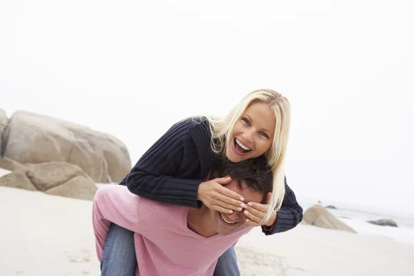 Homem dando mulher piggyback no inverno praia — Fotografia de Stock