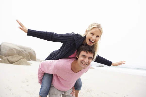 Mannen ger kvinnan piggyback på vintern beach — Stockfoto