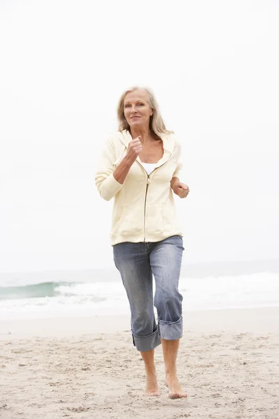 Mulher sênior em férias correndo ao longo da praia de inverno — Fotografia de Stock