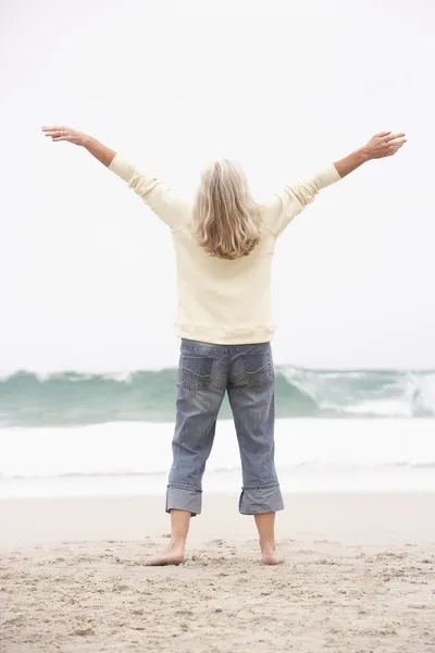 Äldre kvinna med armarna utsträckta på vintern beach — Stockfoto