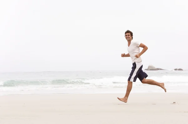 年轻男子沿着冬季海滩跑 — 图库照片