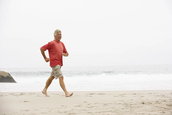 Starszy człowiek na wakacjach działa wzdłuż plaży zima — Zdjęcie stockowe