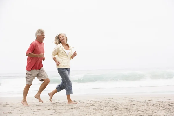 Старшая пара в отпуске, бегущая вдоль Зимнего пляжа — стоковое фото
