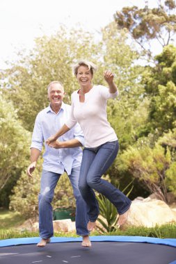 Couple Jumping On Trampoline In Garden clipart