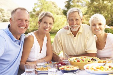 Adult Son And Daughter Enjoying Meal In Garden With Senior Paren clipart