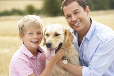 Father And Son Sitting With Dog On Straw Bales In Harvested Fiel clipart