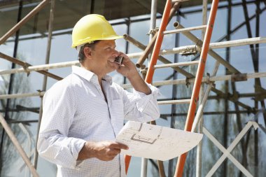 Architect With Plans Outside New Home Talking On Mobile Phone clipart