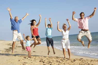 Portrait Of Three Generation Family On Beach Holiday Jumping In clipart