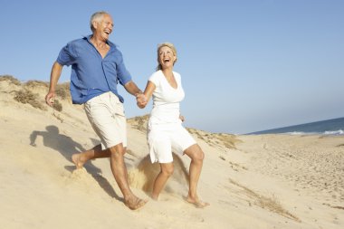 Senior Couple Enjoying Beach Holiday Running Down Dune clipart
