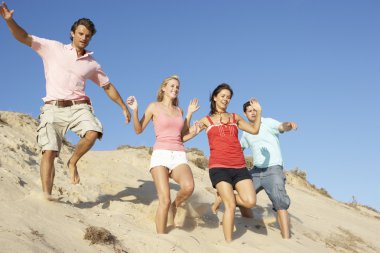 Group Of Friends Enjoying Beach Holiday Running Down Dunes clipart