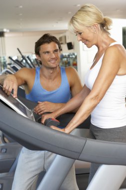 Senior Woman Working With Personal Trainer On Running Machine In clipart