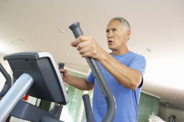 Senior Man On Cross Trainer In Gym clipart