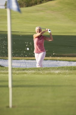 Senior Female Golfer Playing Bunker Shot On Golf Course clipart