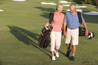 Senior Couple Walking Along Golf Course Carrying Bags clipart