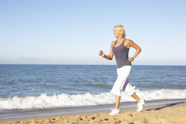 Senior Woman In Fitness Clothing Running Along Beach clipart