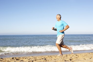 Senior Man In Fitness Clothing Running Along Beach clipart