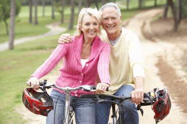 Senior couple riding bicycle in park clipart