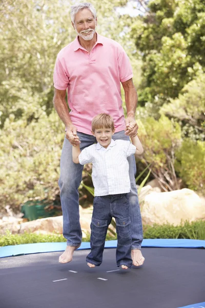 Bedstefar og barnebarn hoppe på trampolin i haven - Stock-foto