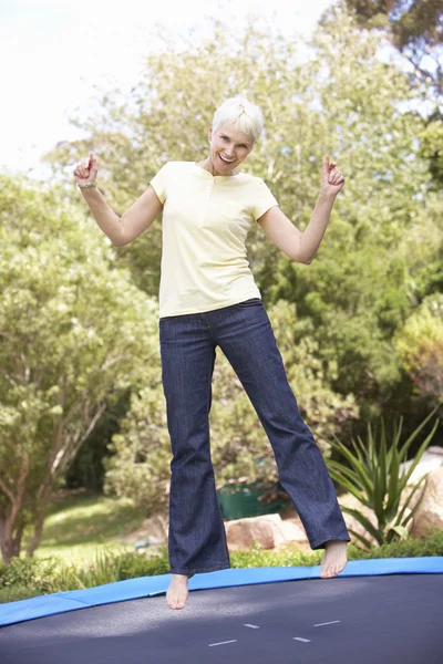Старшая женщина прыгает на батуте в саду — стоковое фото