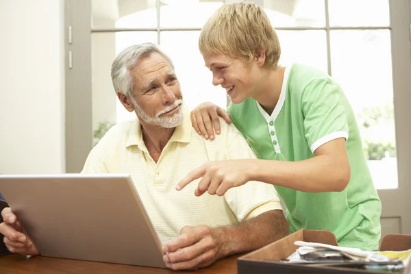 代の孫の祖父はノート パソコンを自宅で使用する支援 — ストック写真