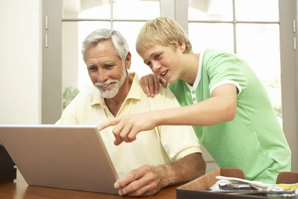Adolescence petit-fils aider grand-père à utiliser un ordinateur portable à la maison — Photo