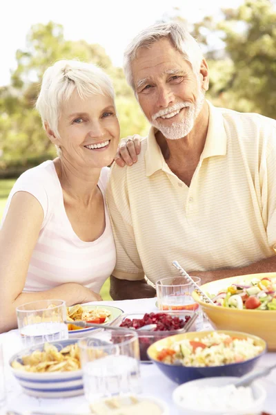 Пара пожилых людей наслаждается едой в саду — стоковое фото