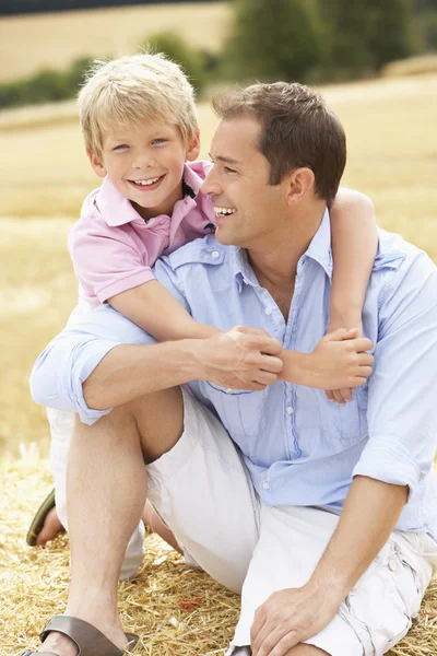 Ojciec i syn siedzi na bele słomy w dziedzinie zbiorów — Zdjęcie stockowe