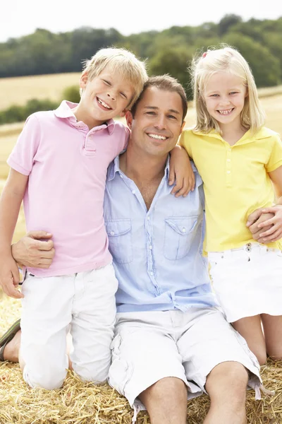Отец и дети, сидящие на соломенных тюках на собранном поле — стоковое фото