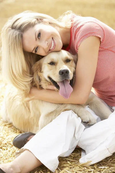 収穫フィールドにわら俵の上に犬と一緒に座っている女性 — ストック写真