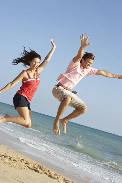 年轻夫妇享受海滩度假在空气中跳跃 — 图库照片