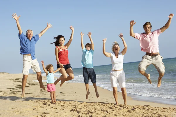 Retrato de la familia de tres generaciones en vacaciones de playa saltando en — Foto de Stock
