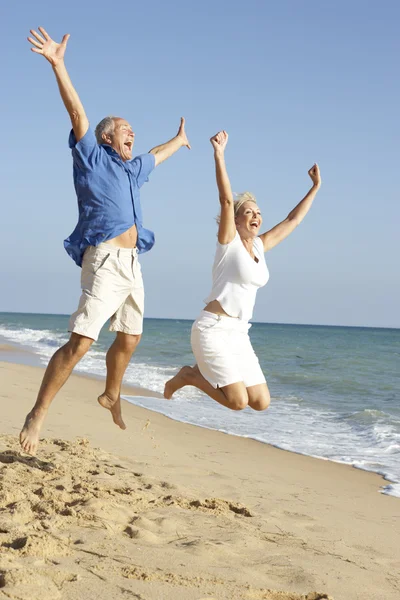 高级夫妇享受海滩度假在空气中跳跃 — 图库照片