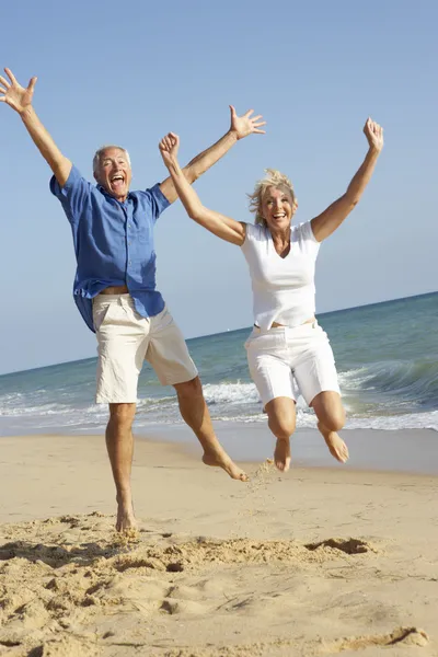 高级夫妇享受海滩度假在空气中跳跃 — 图库照片