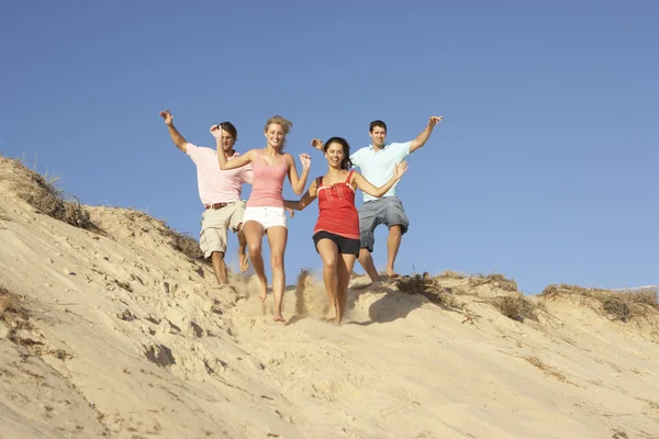 Grupo de amigos disfrutando de vacaciones en la playa corriendo por las dunas — Foto de Stock