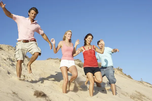 Группа друзей наслаждается пляжным отдыхом, бегущим по дюнам — стоковое фото