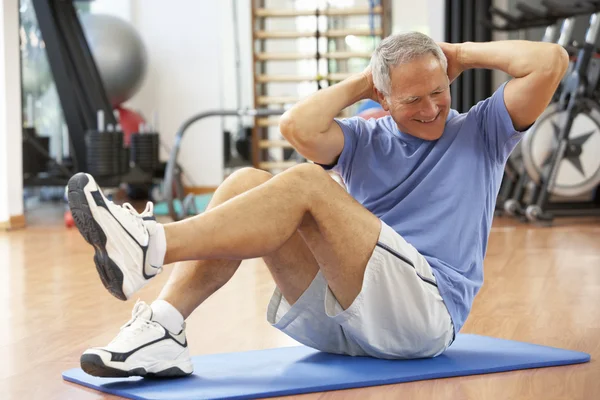 Starszy człowiek robi siedzieć ups w siłowni — Zdjęcie stockowe