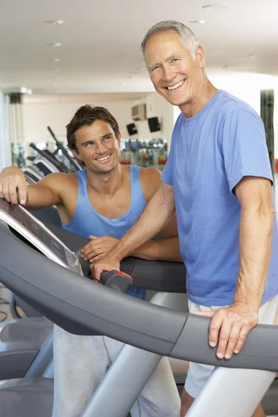 Man aan het werk voor het uitvoeren van de machine in de fitnessruimte met personal trainer — Stockfoto