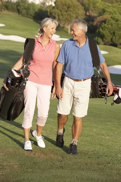 Coppia anziana che cammina lungo il campo da golf portando borse — Foto Stock