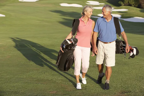 袋を運ぶゴルフ コースに沿って歩いて年配のカップル — ストック写真