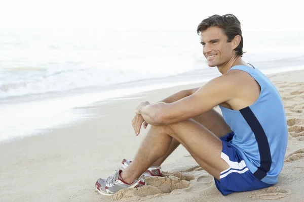 Jonge man in fitness kleding rusten na het sporten op strand — Stockfoto
