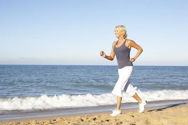 Äldre kvinna i fitness kläder går längs stranden — Stockfoto
