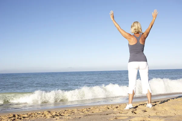 Starší žena v fitness oblečení strečink na pláži — Stock fotografie